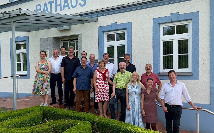 Gruppenfoto von mehreren Personen vor dem Eingang des Rathauses (Schriftzug &bdquo;RATHAUS&ldquo;), stehend auf den Treppenstufen vor der Fassade mit blauen Fensterrahmen.